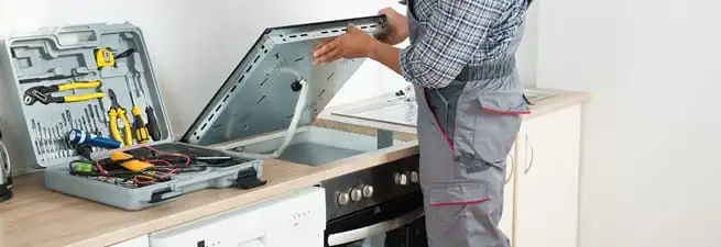 Cooktop repair technician lifting a built-in stovetop for service in San Jose, CA