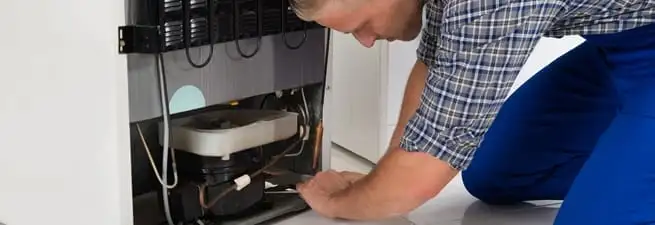 Refrigerator repair technician servicing the compressor and condenser area in San Jose, CA