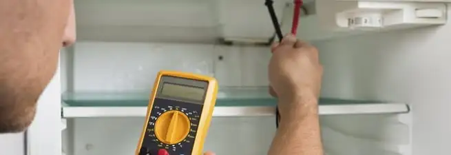 Refrigerator repair technician testing electrical components with a multimeter in San Jose, CA